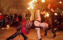 Eine luftig gekleidete Feuerkünstlerin, assistiert von ihrem Partner in Lack und Leder.