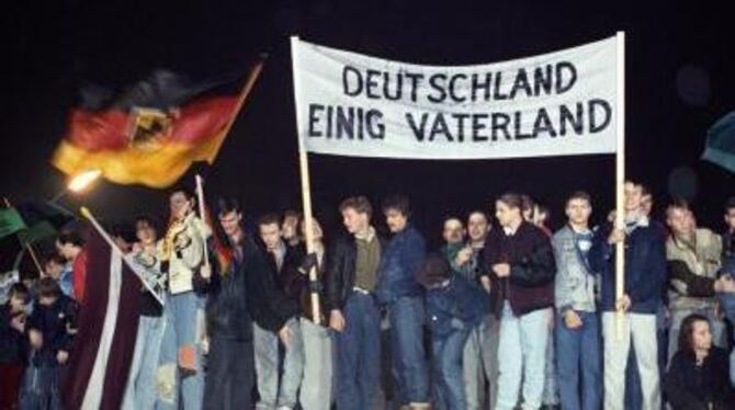 Mit der Deutschlandfahne und einem Transparent »Deutschland einig Vaterland« stehen Berliner am 1989 auf der Mauer am Brandenbur