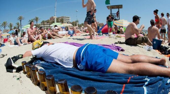Ausgetrunken: Ein Tourist schläft neben leeren Bierflaschen am Strand von Arenal. Foto: Julian Stratenschulte/Archiv
