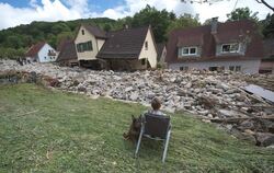 Ein junger Mann sitzt mit seinem Hund in Braunsbach vor einer Gerölllawine.