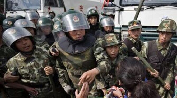 Eine zur Minderheit der muslimischen Uiguren gehörende Frau stemmt sich mit aller Kraft gegen das chinesische Militär.
FOTO: DPA