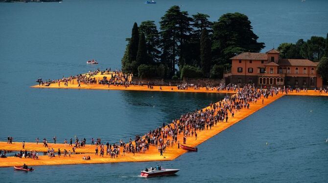 Besucher gehen über orangefarbenen Stoff auf schwimmenden Stegen vor Paratico im Rahmen des Projekts »The Floating Piers« von Ch