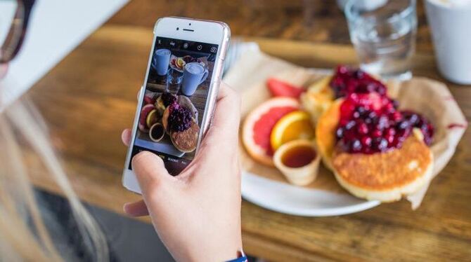 So schmeckt es manchen noch besser: Eine junge Frau fotografiert mit einem Smartphone ihr Essen. Foto: Sophia Kembowski