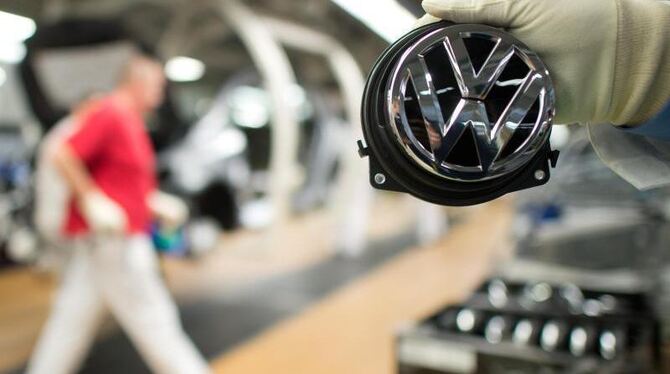 Ein Mitarbeiter zeigt in Wolfsburg ein Volkswagen-Logo. Foto: Foto: Julian Stratenschulte